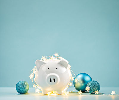 White Piggy bank wrapped in a string of Christmas lights over a blue background. Saving concept.
