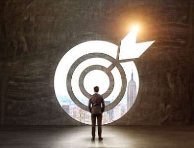 A businessman with hands in pockets standing in front of a target through which he can see New York.