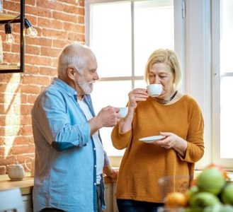 Senior couple having a coffee time, standing together near the window on the kitchen at home