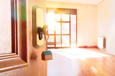 Open entrance door detail of a house with keys in the lock and empty room in the background with golden light effect. Lateral view