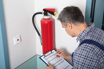 Close-up Of A Male Professional Checking A Fire Extinguisher Using Clipboard