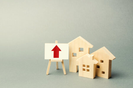 three wooden houses and a red up arrow on the sign. Real estate value increase. High rates of construction, high liquidity. Supply and demand. Rising prices for housing, building maintenance.