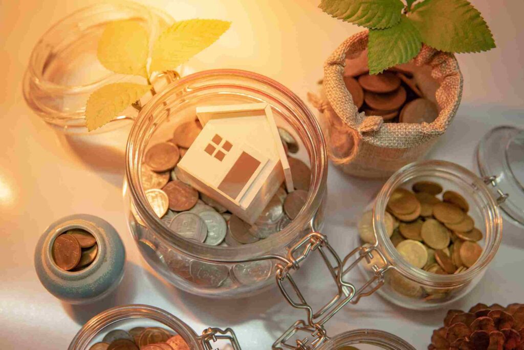 A wooden house model resting on top of a pot of money representing property savings.