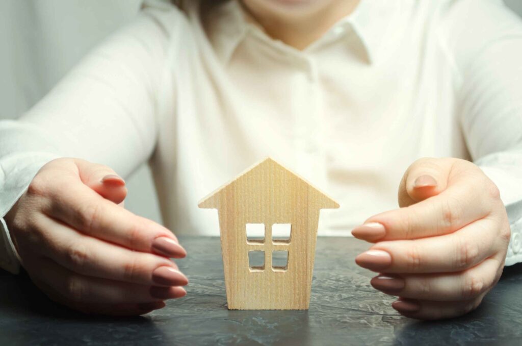 A woman's hands either side of a house model representing property advice.
