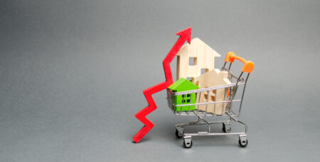 Wooden houses in a shopping cart and red arrow up. The concept of increasing the cost of housing. High demand for real estate. The growth of rent and mortgage rates. Sale of apartments