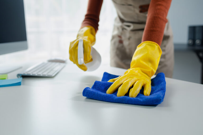 Cleaning desk surface in office with sanitizer spray, wear glove